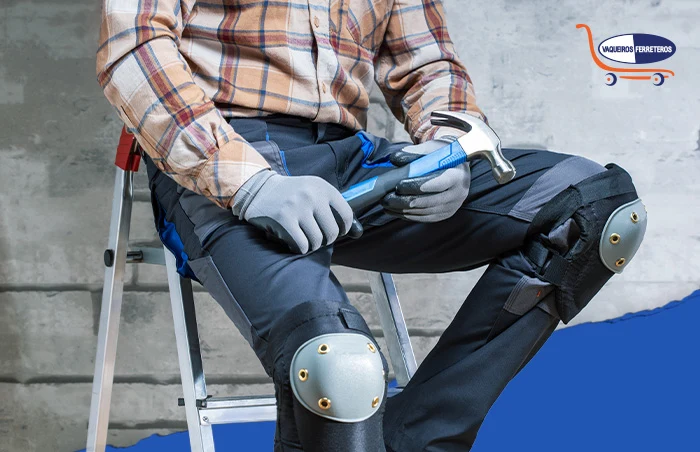Trabajador sentado sobre los peldaños de una escalera de aluminio. Trae puestas unas rodilleras, guantes y sostiene un martillo.