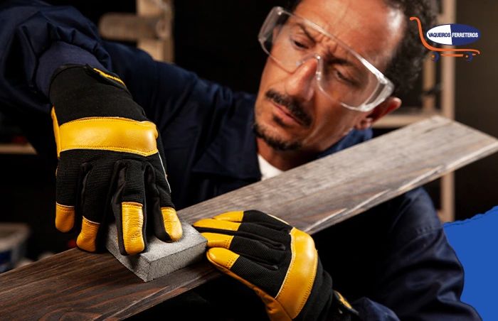 Persona lijando una tabla de madera, usa distintos tipos de equipo de protección personal como guantes, gafas y overol.