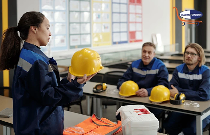 Mujer instruyendo a dos trabajadores sobre equipo de seguridad. Muestra un casco amarillo entre sus manos a los trabajadores mientras ellos ponen atención.