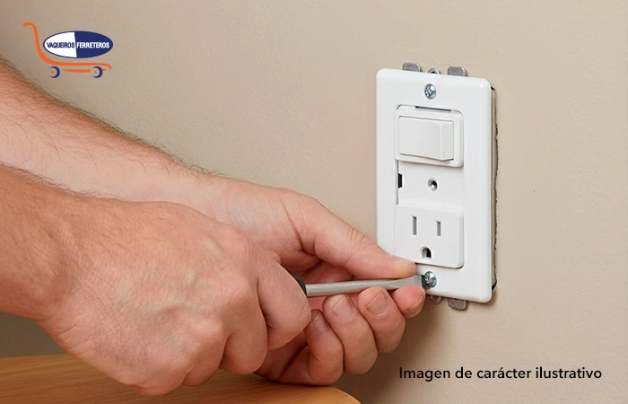 Manos atornillando la tapa de un apagador y contacto en la pared.